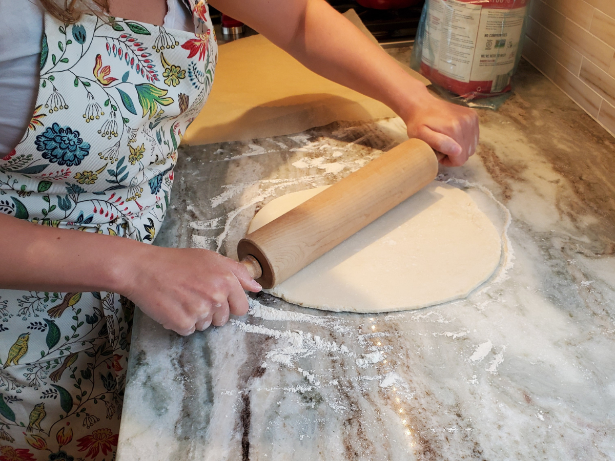 joey rockman rolling out pie dough wearing a floral apron